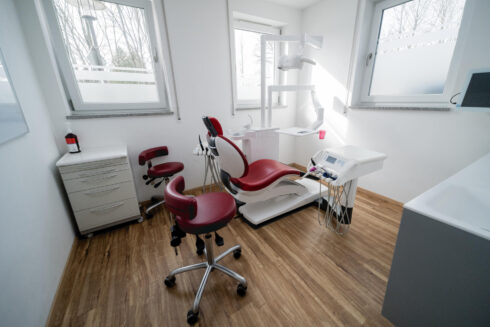 Aufnahme aus der Ecke vom kleinen Behandlungszimmer mit rotem Zahnarztstuhl ohne Personen