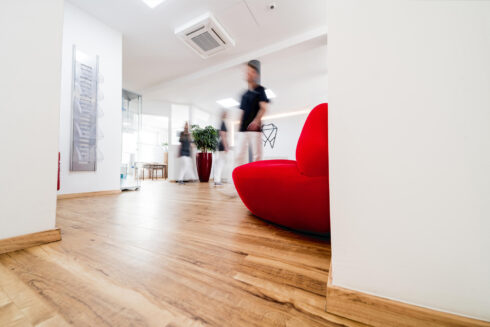 Praxisflur mit roter Lippencouch aus der Froschperspektive. Bewegungsunschärfe der durch den Flur laufenden Angestellten