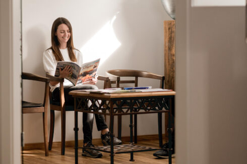 Dunkelhaarige, junge Patientin sitzt im Wartezimmer und liest eine Zeitschrift