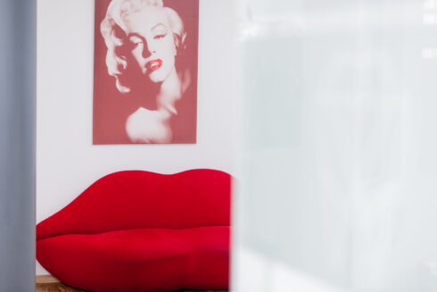 Praxisflux mit Vorderansicht auf rotes Lippensofa. Darüber hängt ein Bild von Marilyn Monroe